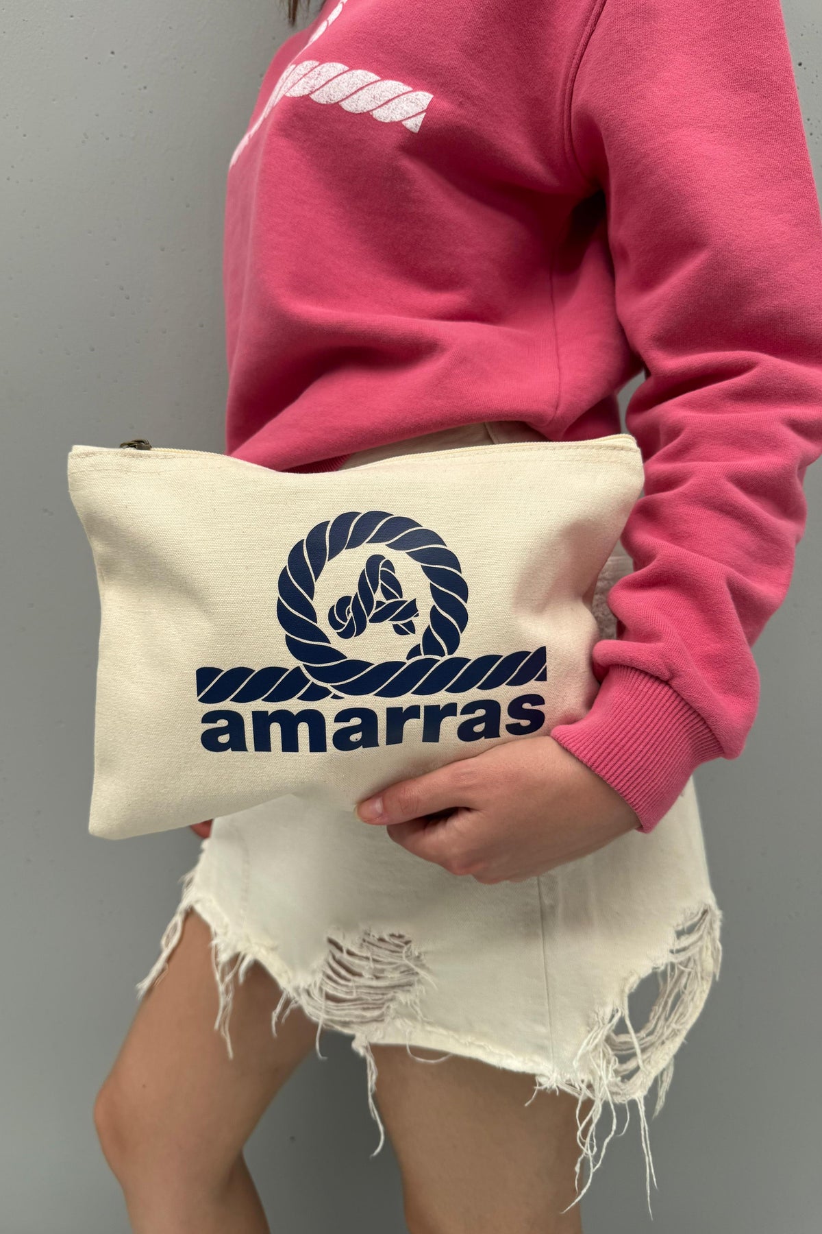 Mujer sosteniendo el bolso Tulum de loneta cruda, con cierre de cremallera y logotipo Amarras azul marino.