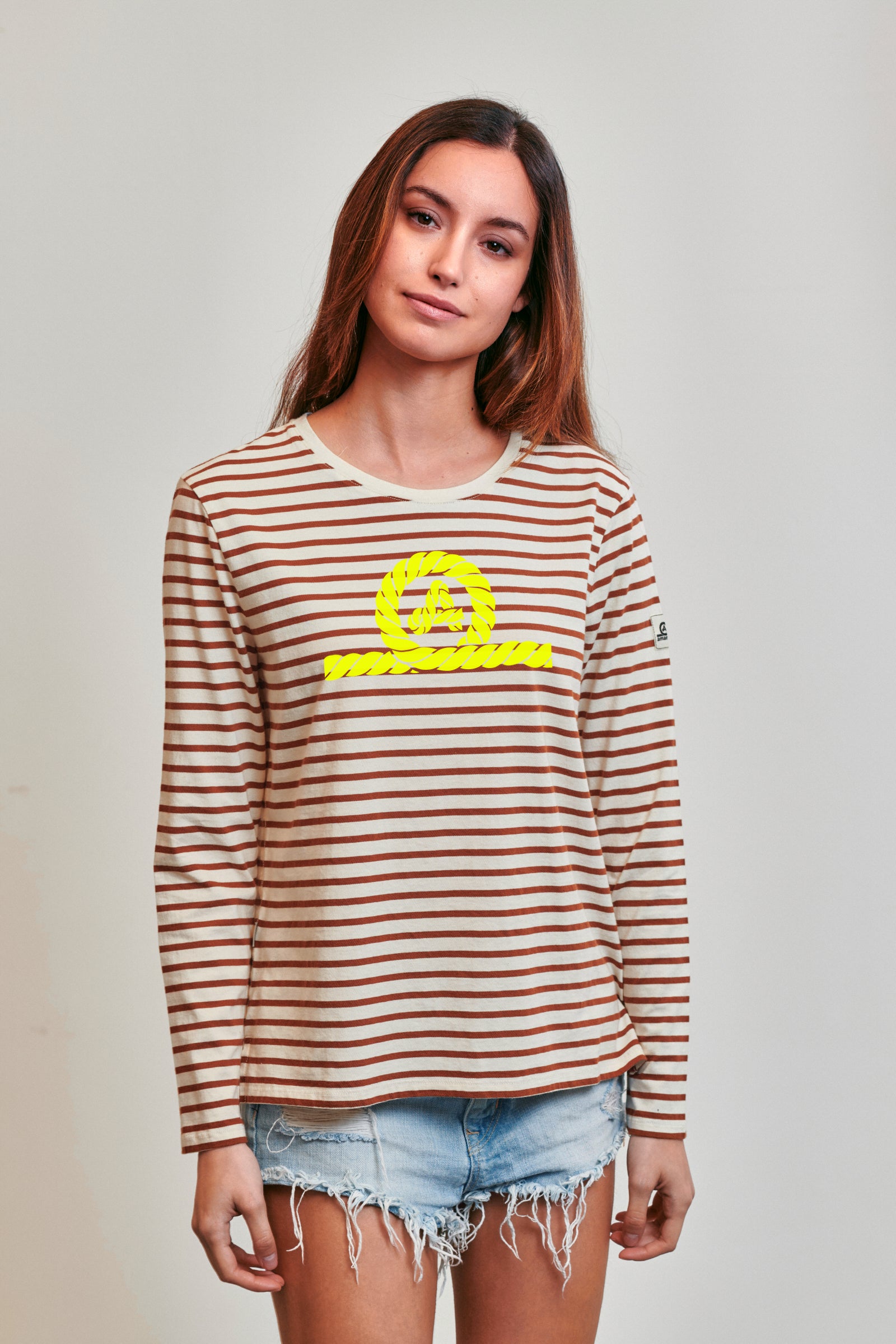 Camiseta de manga larga modelo Riva para mujer de Amarras, con diseño de rayas marrones y logo central en amarillofluor.
