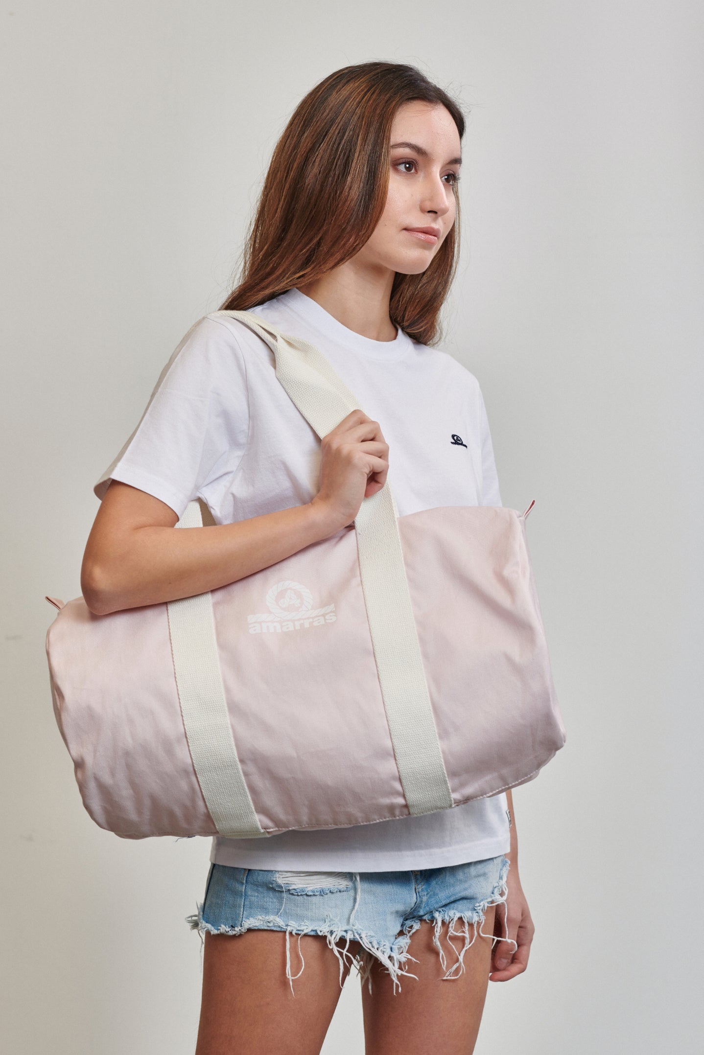 Bolsa tipo duffle de lona azul marino con asas de algodón crudo y logotipo clásico de Amarras, llevada por modelo con camiseta blanca.