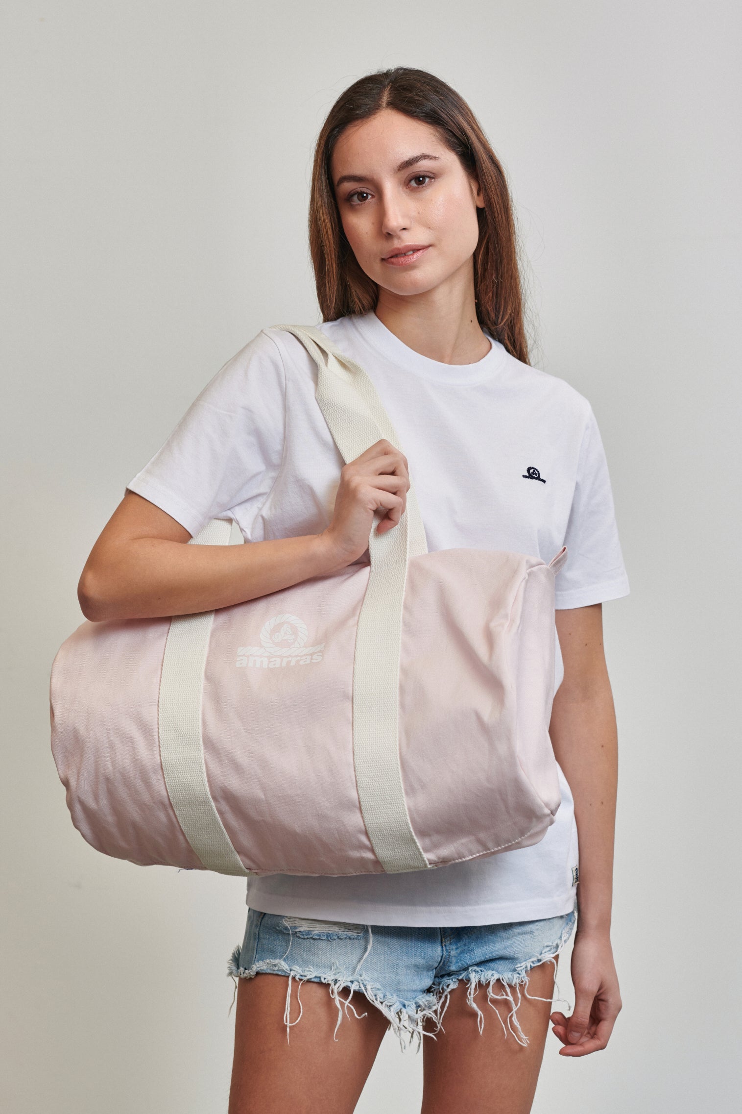 Bolsa tipo duffle de lona azul marino con asas de algodón crudo y logotipo clásico de Amarras, llevada por modelo con camiseta blanca.