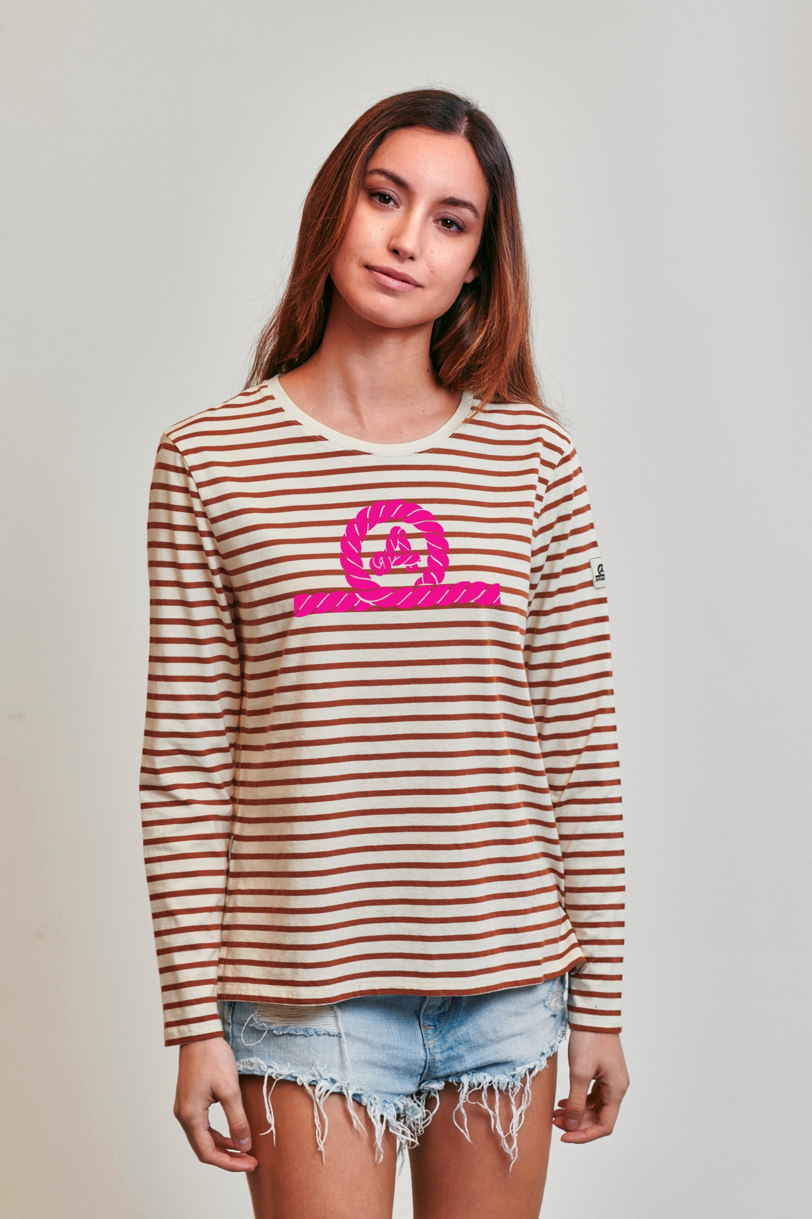 Camiseta de manga larga modelo Riva para mujer de Amarras, con diseño de rayas marrones y logo central en rosa fluor.
